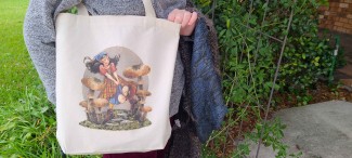 A natural cotton tote bag featuring a Renn Faire or fantasy inspired girl running through oversized mushrooms.  She wears a kerchief and a plaid skirt, and her hair is floating behind her.